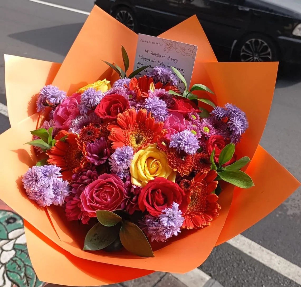 A Bali Bright Bunch photographed in the Seminyak shop before delivery, orange gerberas, blue-purple irises, closed yellow lily buds and red roses hand-tied in kraft paper with a coral ribbon